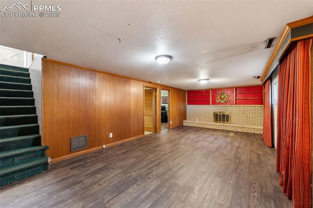 Image 27 of 49: Unfurnished living room with wooden walls, dark wood-style floors, a textur