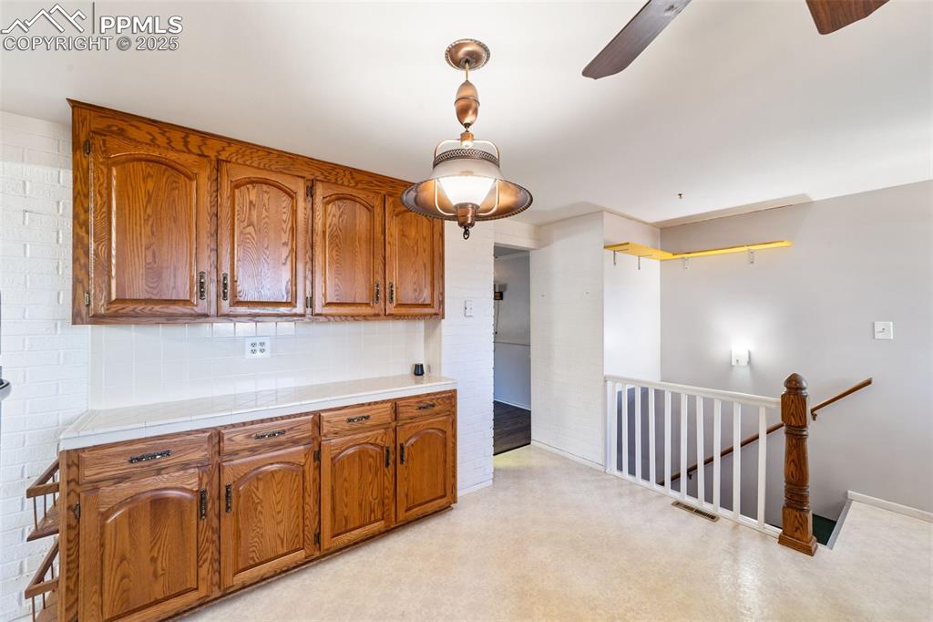 Image 5 of 49: Kitchen with backsplash, decorative light fixtures, brown cabinetry, tile c