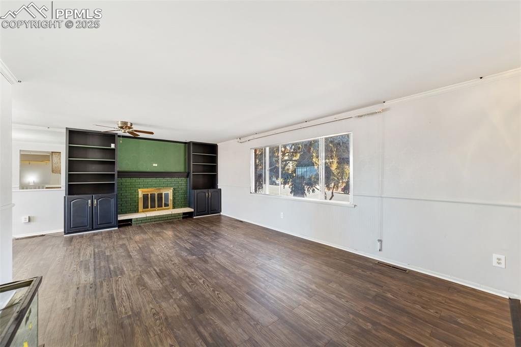 Image 6 of 49: Unfurnished living room featuring dark wood-type flooring, a brick fireplac