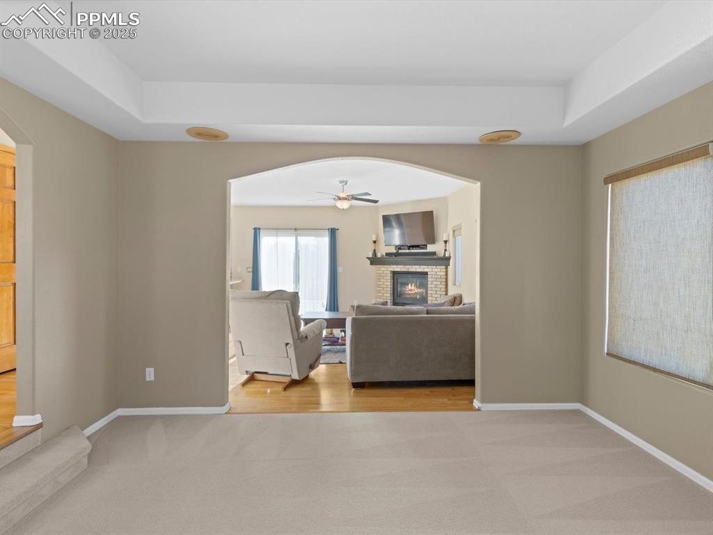 Image 11 of 49: Living area with light carpet, a brick fireplace, a ceiling fan, and arched