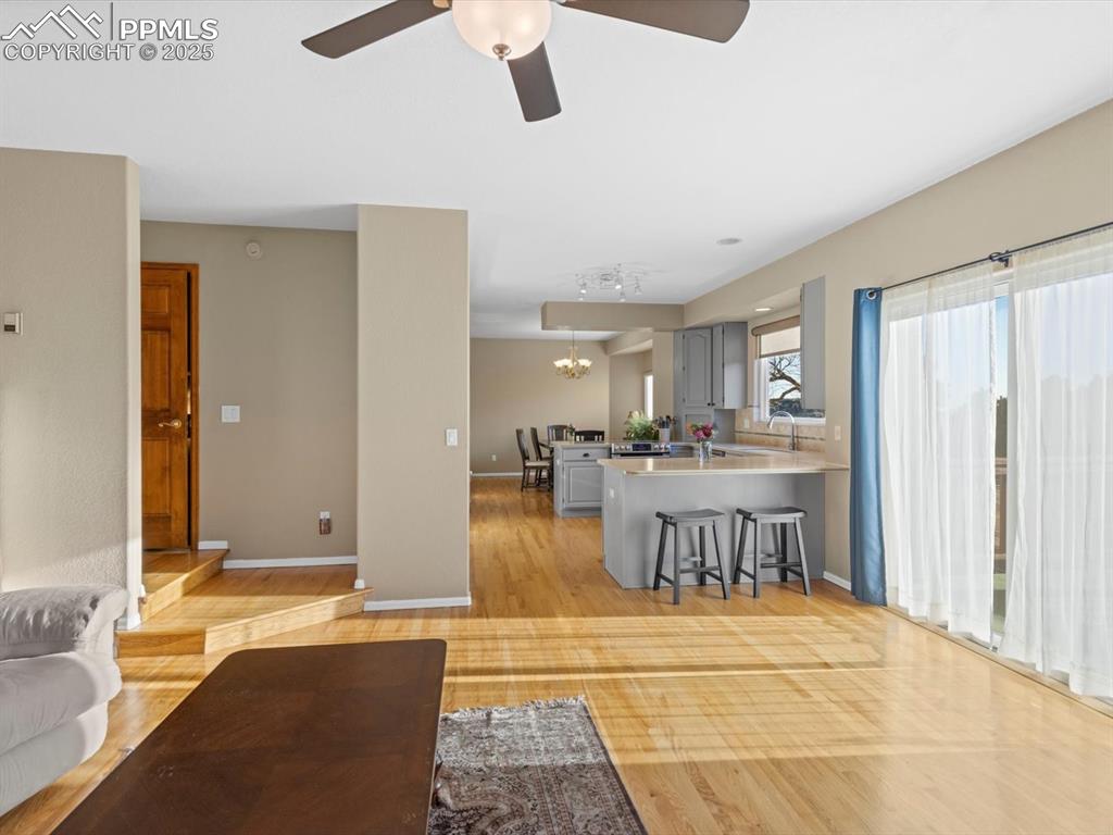 Image 13 of 49: Living room with light wood finished floors, a ceiling fan, and a chandelie