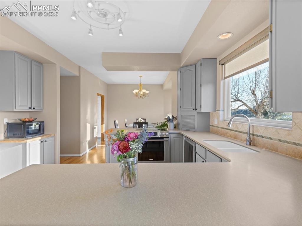 Image 19 of 49: Kitchen featuring gray cabinetry, light countertops, a chandelier, light wo