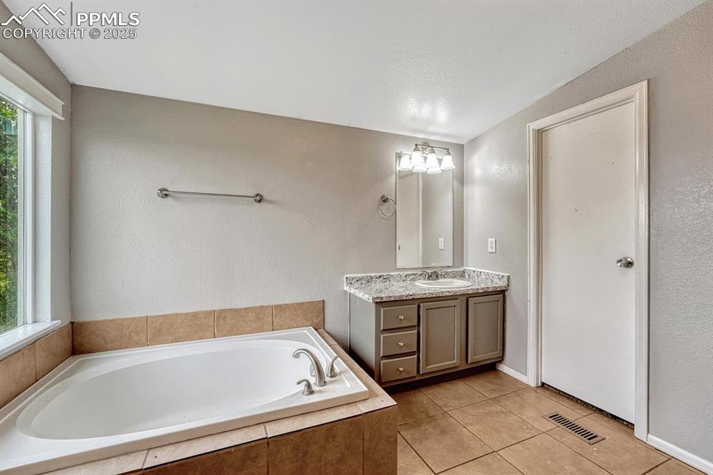 Image 19 of 38: Full bath featuring a textured wall, vanity, a garden tub, light tile patte