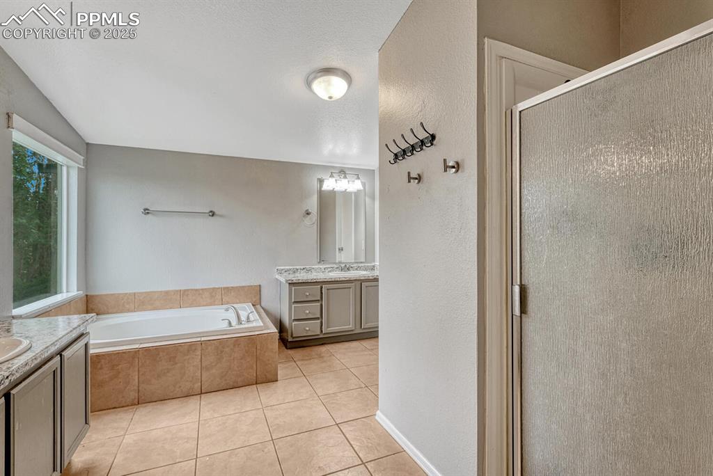 Image 20 of 38: Full bath with two vanities, a stall shower, a bath, light tile patterned f