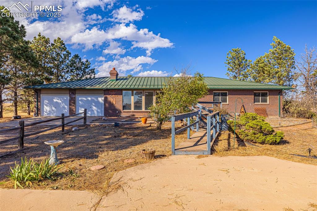 Caption: Single story home featuring brick siding, driveway, a metal roof, a chimney, and a garage