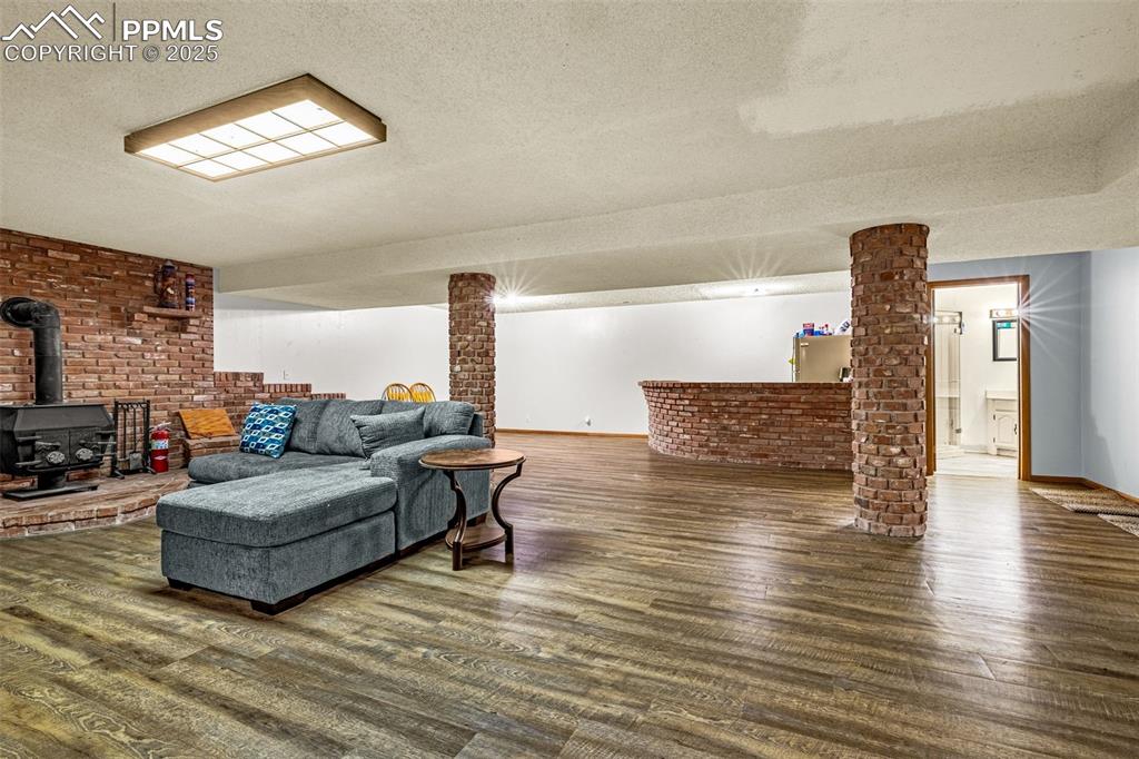 Image 22 of 42: Living area featuring a wood stove, brick wall, a textured ceiling, and woo