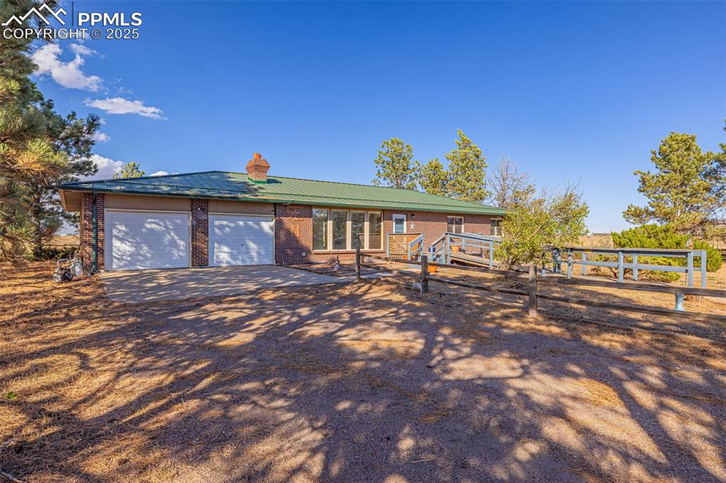 Image 3 of 42: Single story home with a chimney, brick siding, dirt driveway, a metal roof