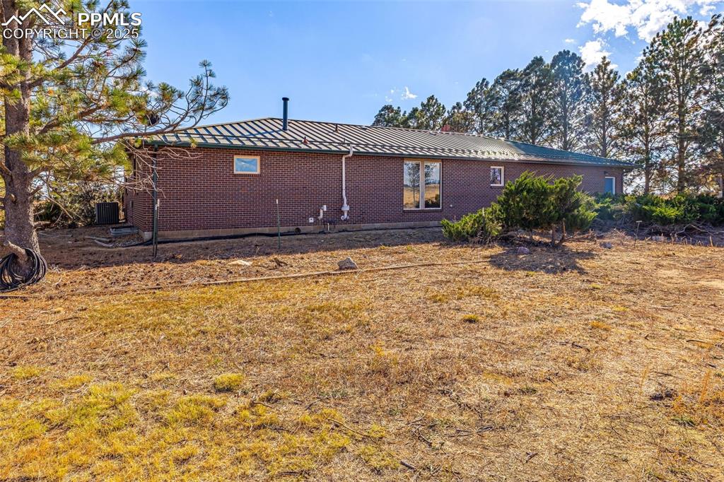 Image 31 of 42: Rear view of house with brick siding, a metal roof, and a yard