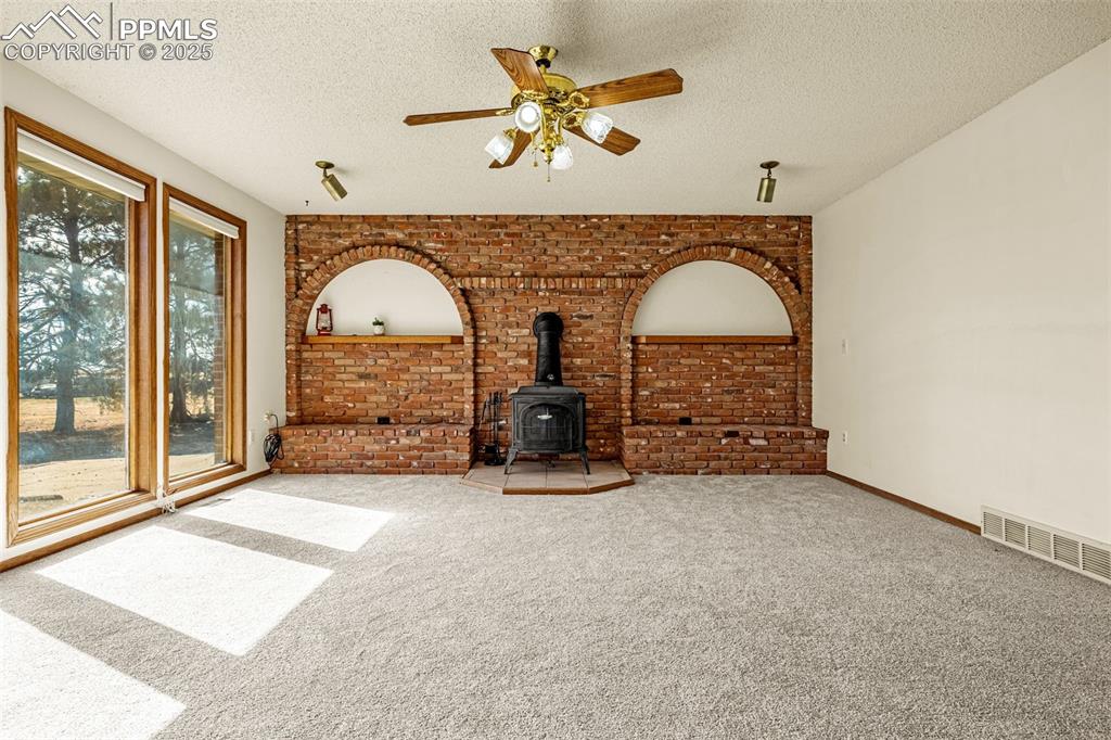 Image 6 of 42: Unfurnished living room with a wood stove, carpet, a ceiling fan, a texture