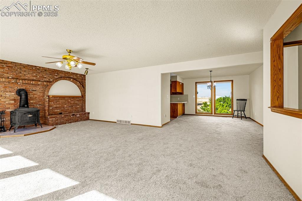 Image 8 of 42: Unfurnished living room featuring a wood stove, light carpet, a textured ce