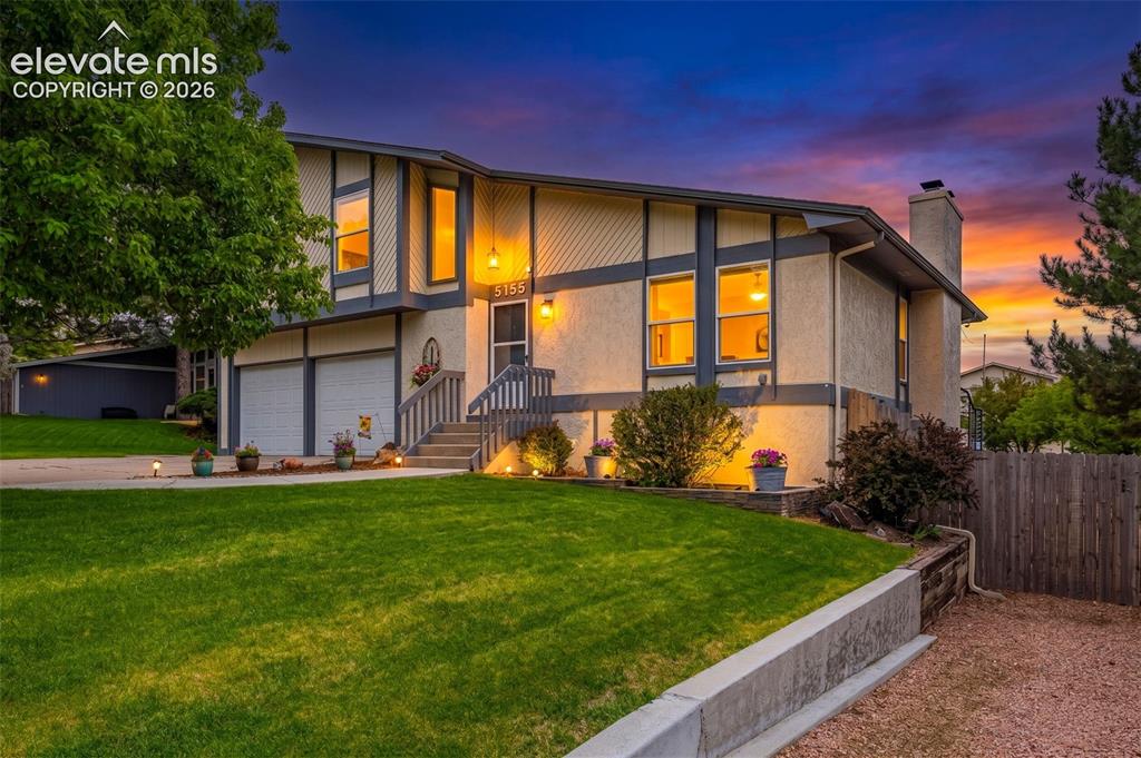 Image 1 of 44: Split-level residence at sunset featuring a stucco and board-and-batten ext