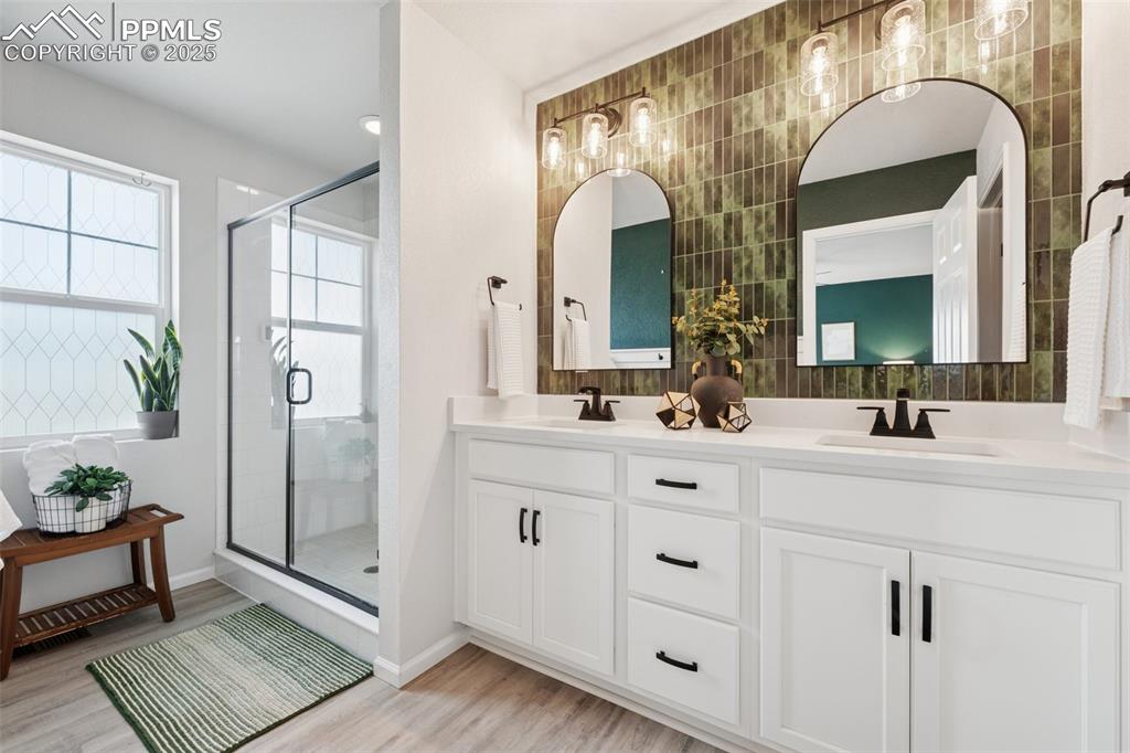 Image 18 of 30: Bathroom featuring wood finished floors, double vanity, a shower stall, and
