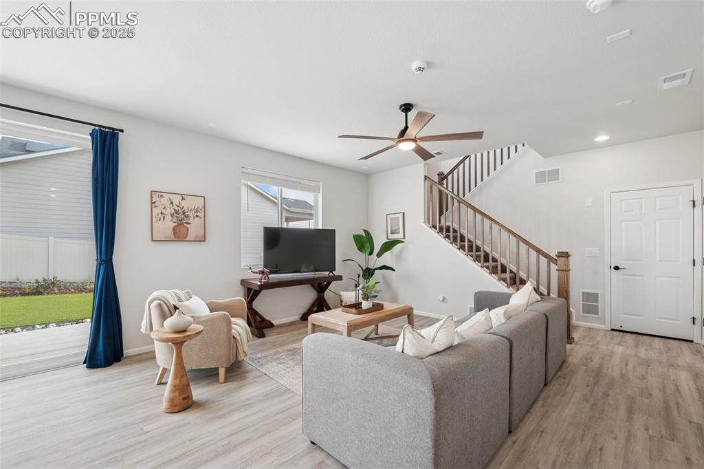 Image 6 of 30: Living area featuring light wood-style floors, ceiling fan, stairway, and r