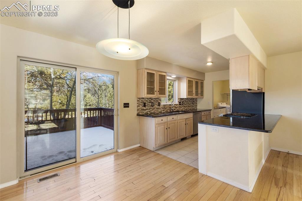 Image 10 of 36: Kitchen with glass insert cabinets, light wood-style floors, tasteful backs