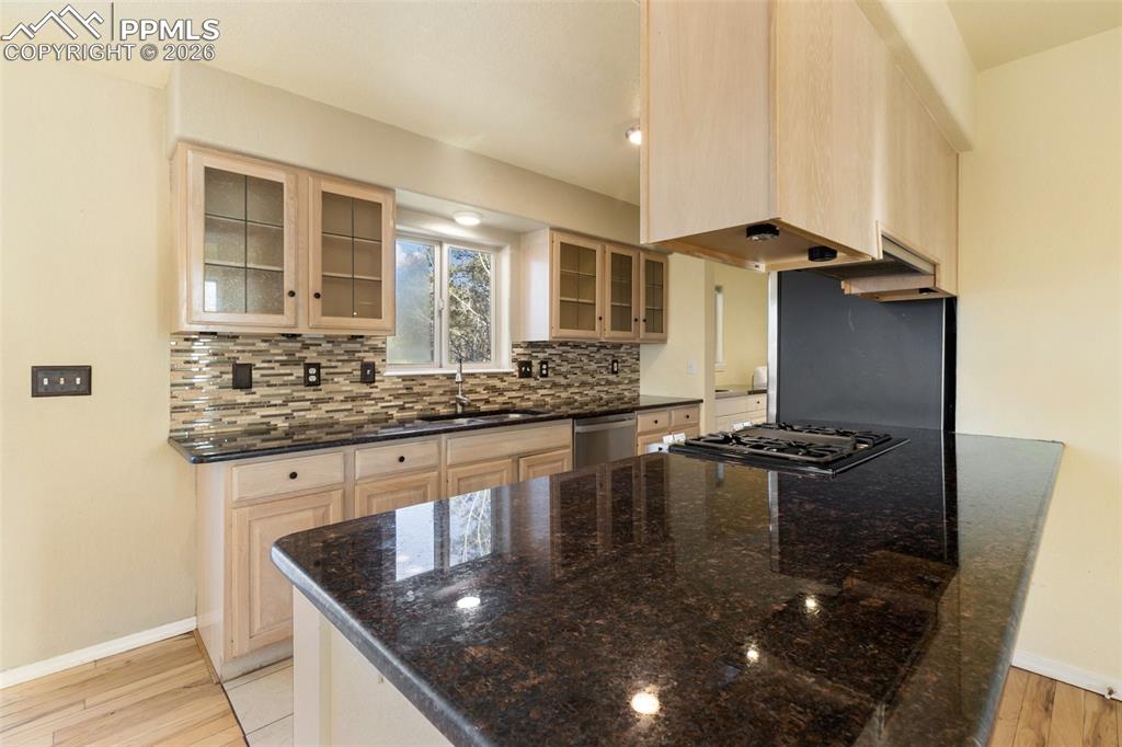 Image 11 of 36: Kitchen with light brown cabinetry, dark stone counters, light wood-type fl