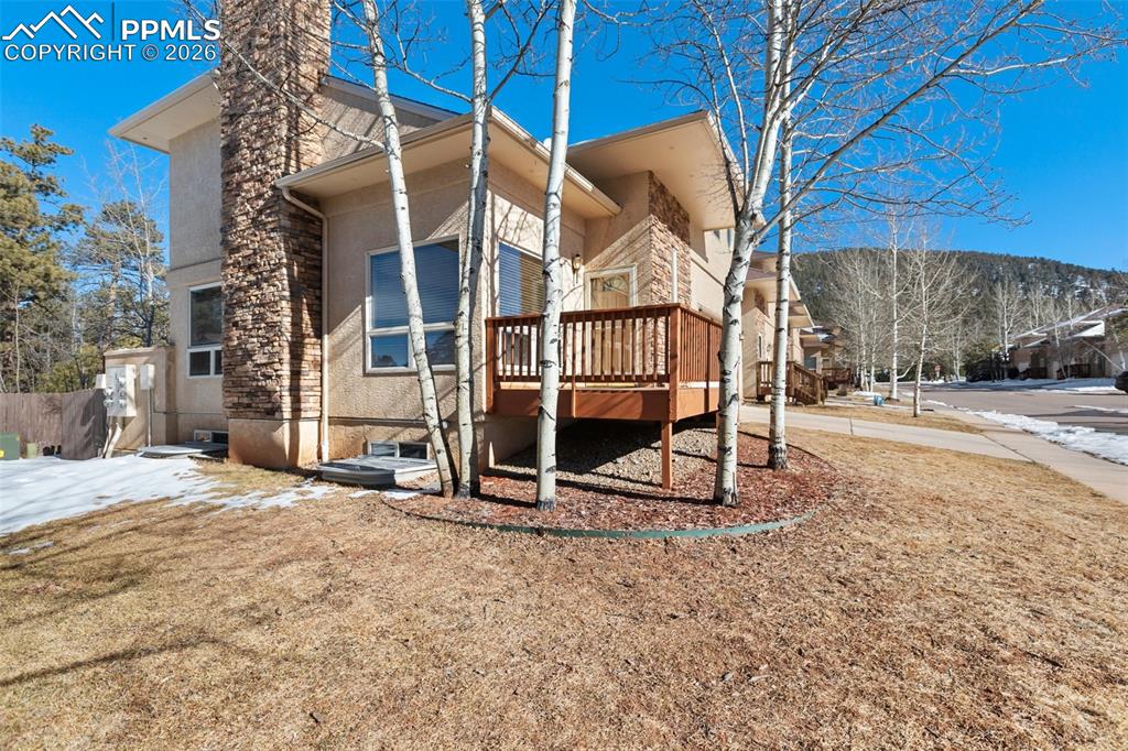 Image 2 of 36: View of side of home with a wooden deck, stucco siding, a chimney, and ston