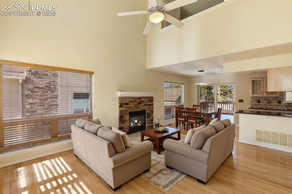 Image 5 of 36: Living area with light wood finished floors, a fireplace, a ceiling fan, an