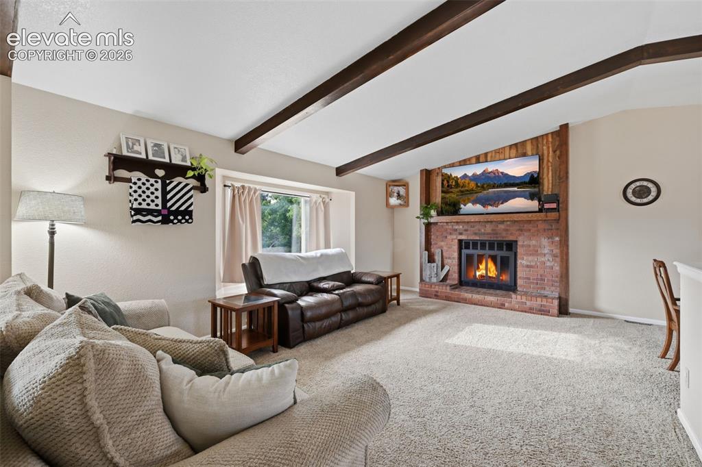 Image 2 of 28: Living space featuring a brick fireplace with wood paneling, exposed beam c