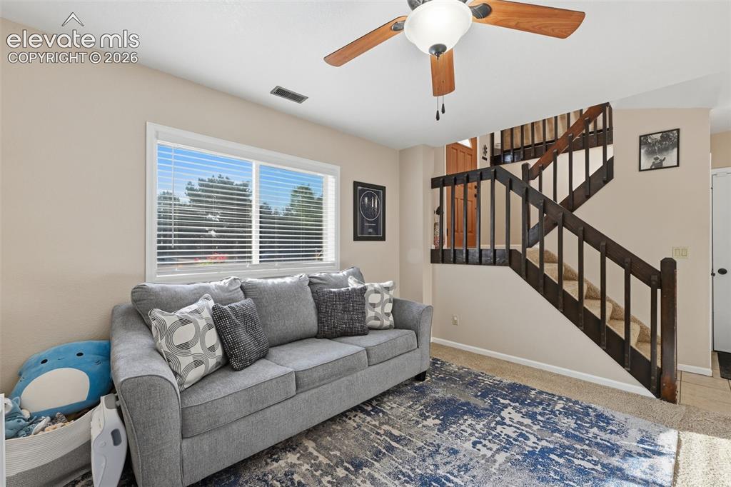 Image 20 of 28: Living area featuring a large window with blinds, a ceiling fan with light