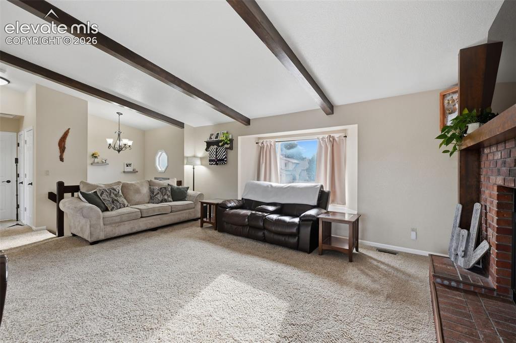 Image 3 of 28: Living area featuring vaulted ceilings with exposed wood beams, a brick-sur