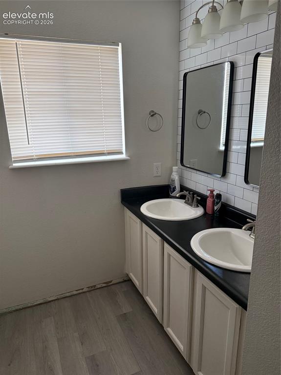 Image 11 of 21: Dual vanity with white shaker-style cabinetry, black countertops, and under
