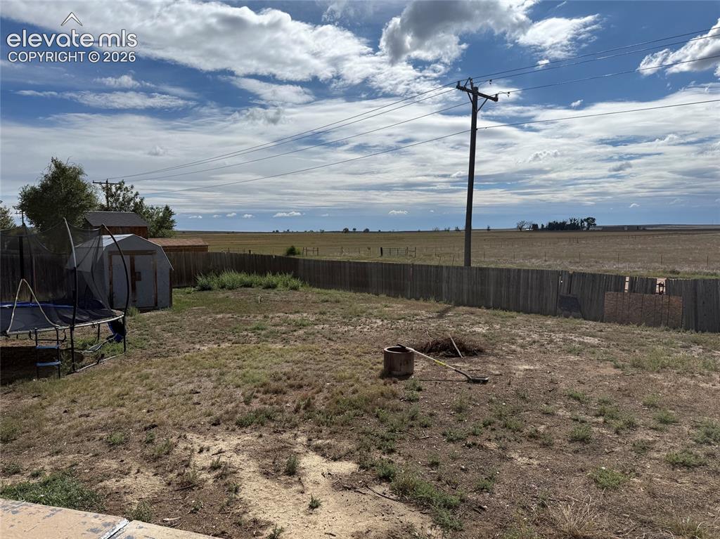 Image 20 of 21: Fenced backyard featuring a storage shed and open land beyond the property 