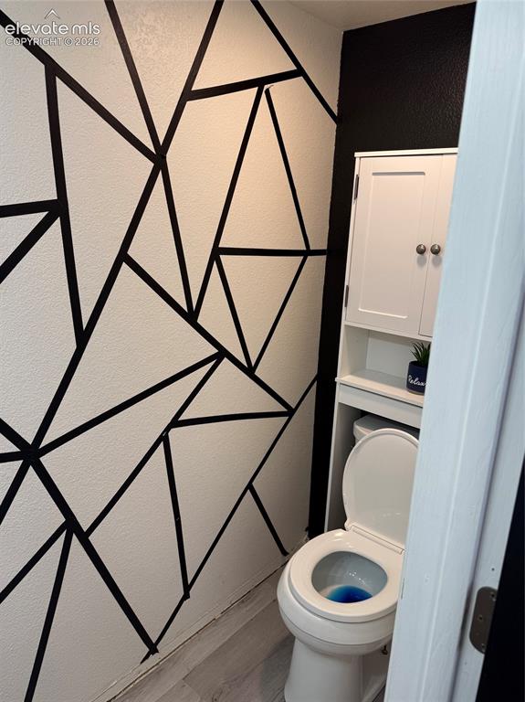 Image 8 of 21: Geometric accent wall, white wall-mounted storage cabinet, white toilet, an