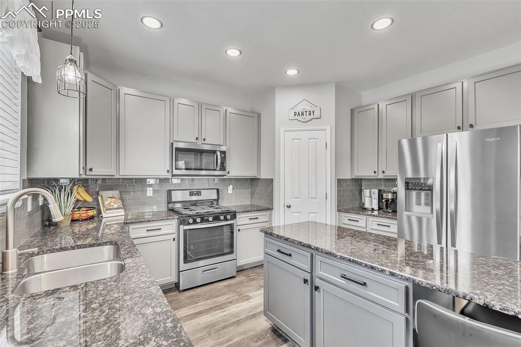 Image 12 of 50: Kitchen with gray cabinetry, stainless steel appliances, pendant lighting, 