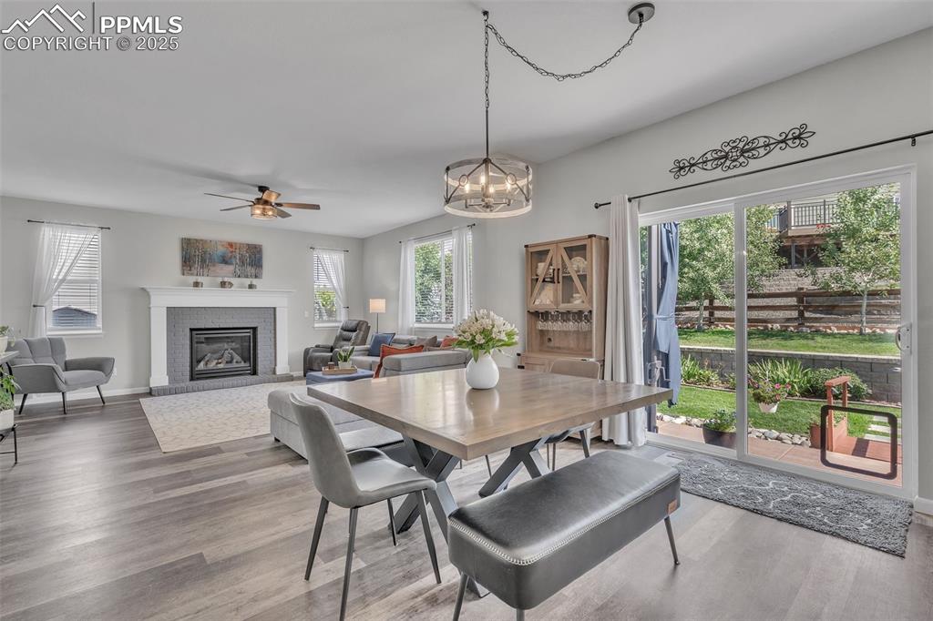 Image 8 of 50: Dining room with wood finished floors, a ceiling fan, a brick fireplace, an