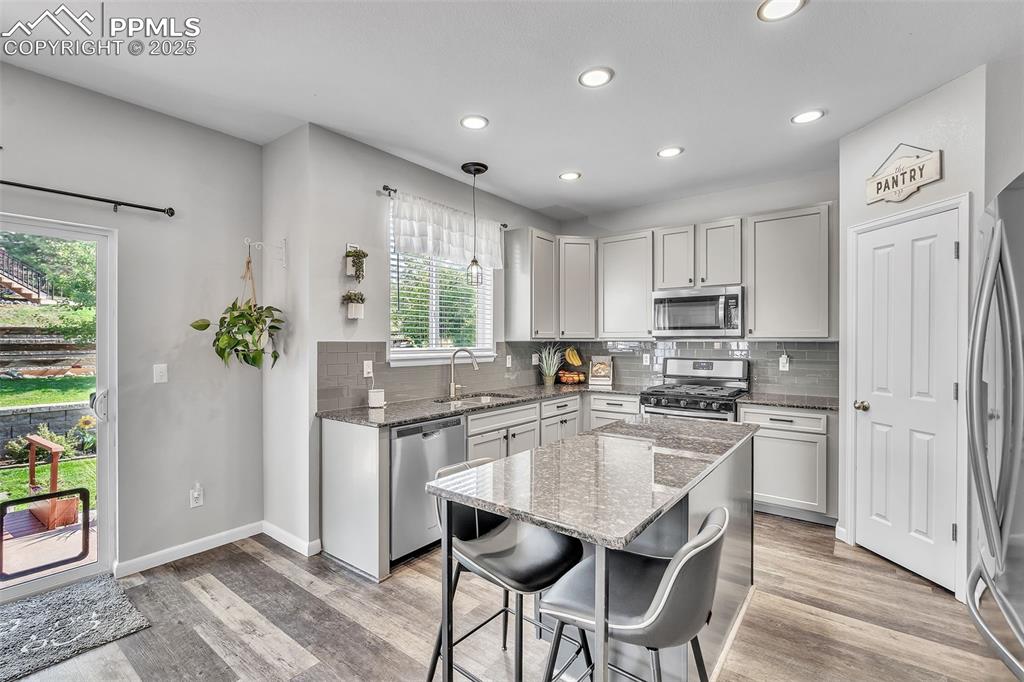 Image 9 of 50: Kitchen with dark stone countertops, decorative light fixtures, gray cabine