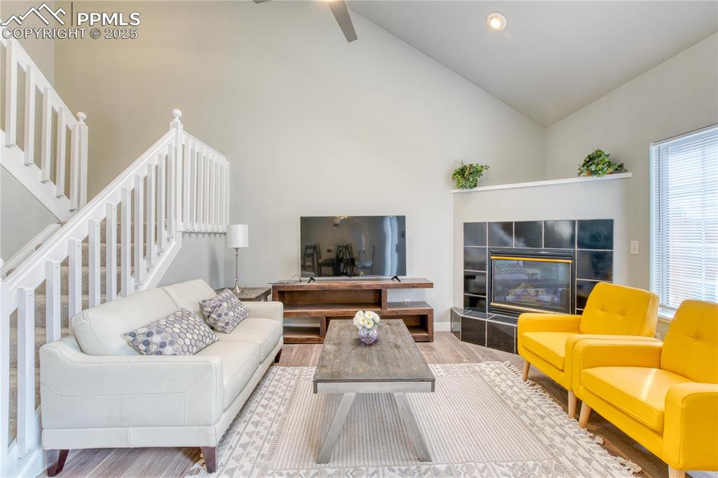 Image 4 of 20: Living room with stairway, high vaulted ceiling, baseboards, a tiled firepl