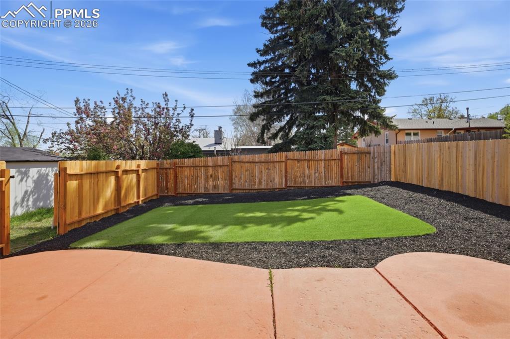 Image 16 of 44: The property features a fenced yard with a concrete patio, a green lawn, an