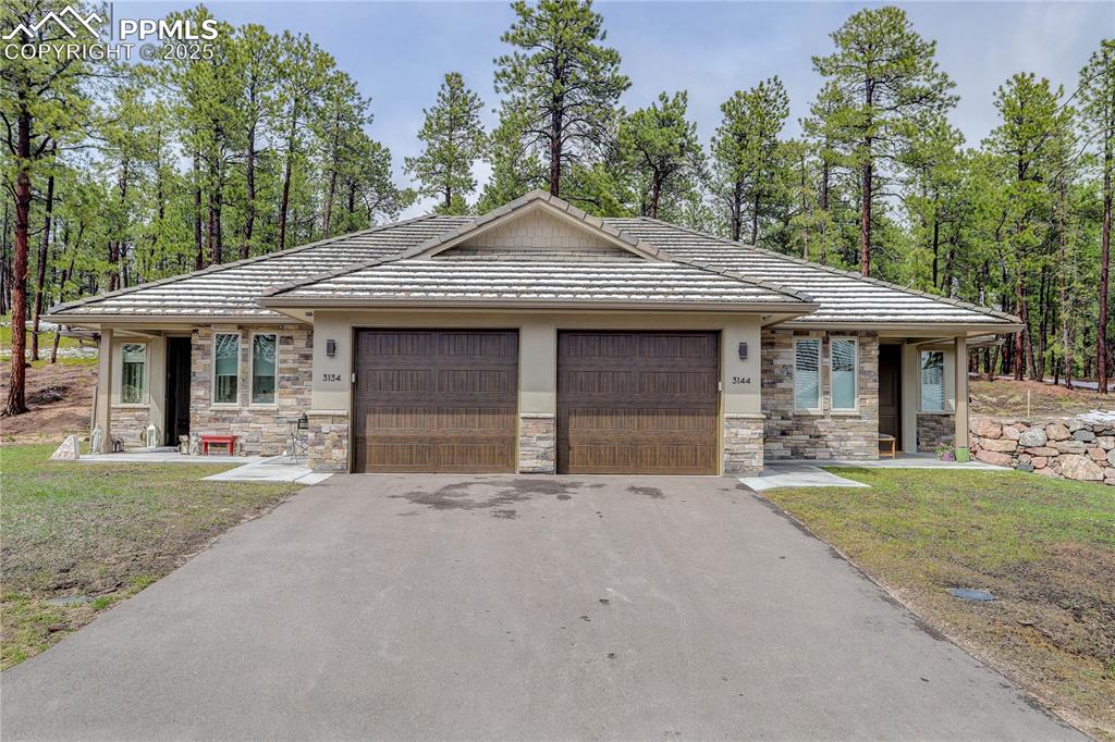 Caption: View of front of property featuring an attached garage, stone siding, a tile roof, and asphalt drive