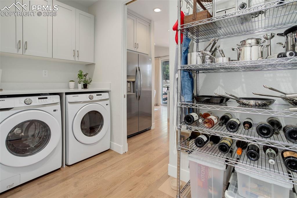 Image 11 of 28: Clothes washing area with washer and dryer, cabinet space, light wood finis