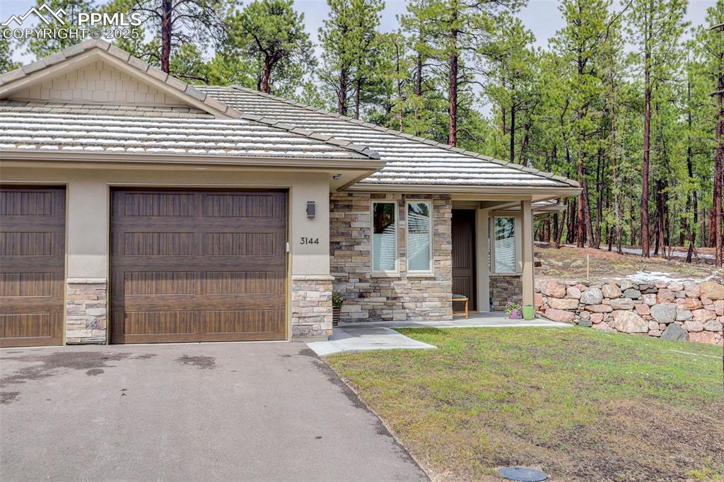 Image 2 of 28: View of front facade featuring stone siding, a tile roof, driveway, and stu