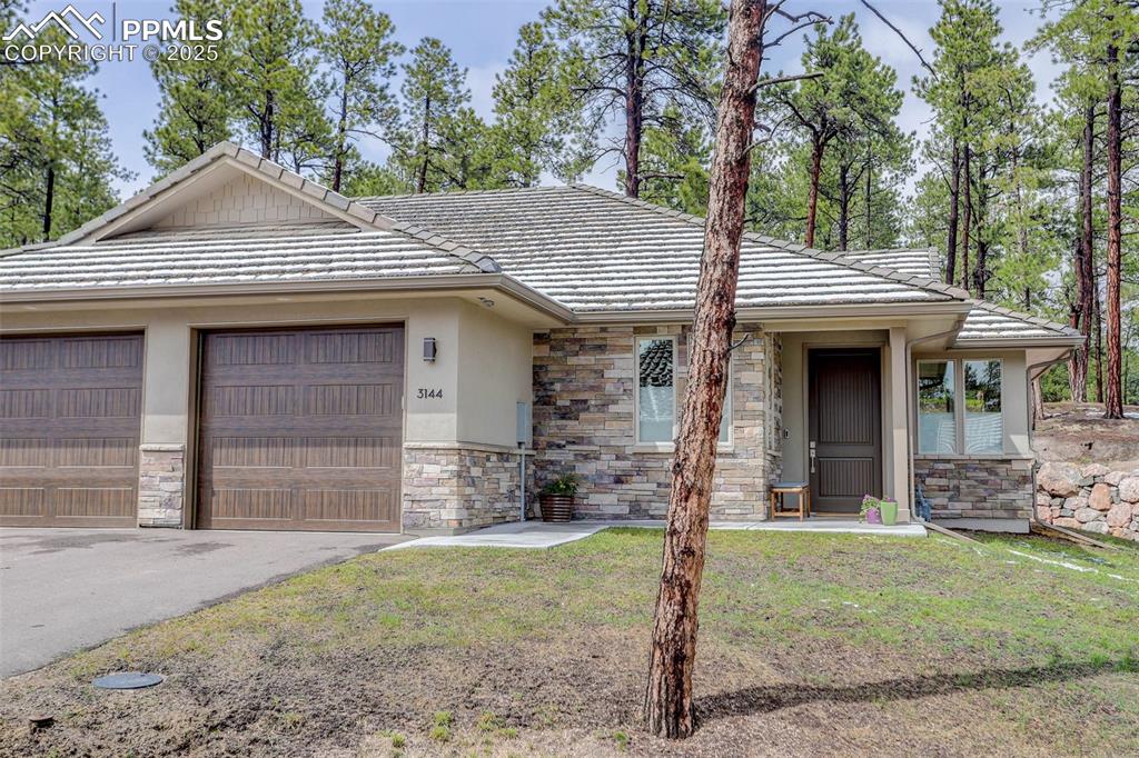Image 3 of 28: View of front of property with stone siding, a tiled roof, asphalt driveway