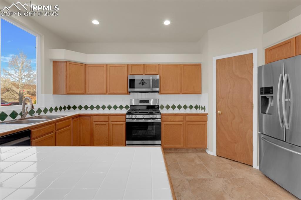 Image 11 of 41: Kitchen with stainless steel appliances, recessed lighting, tile countertop