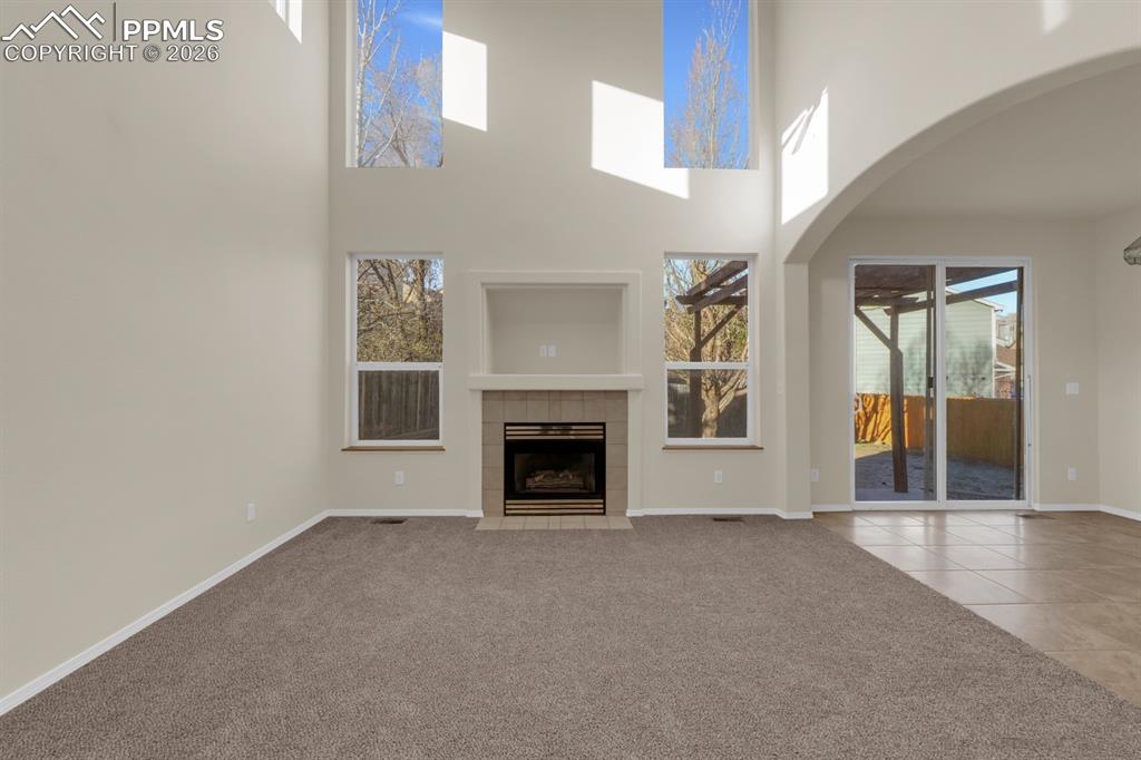 Image 9 of 41: living room featuring light carpet, a high ceiling, a tiled fireplace, arch