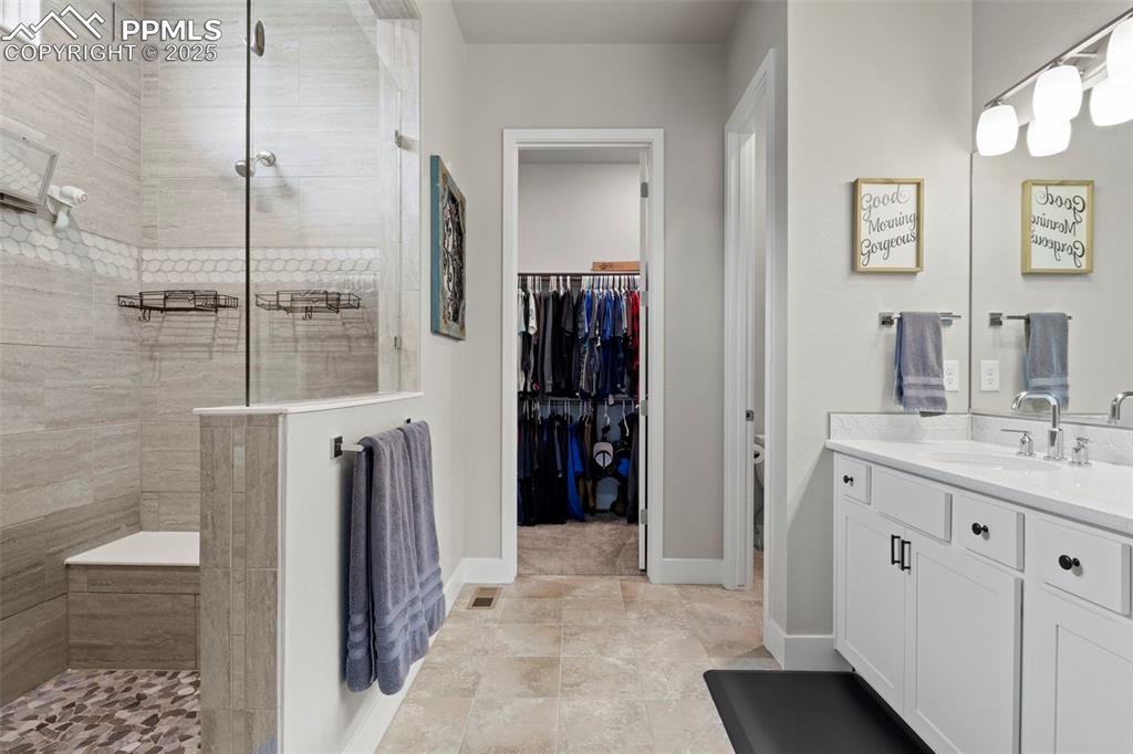 Image 15 of 38: Bathroom with a tile shower, a spacious closet, vanity, and baseboards