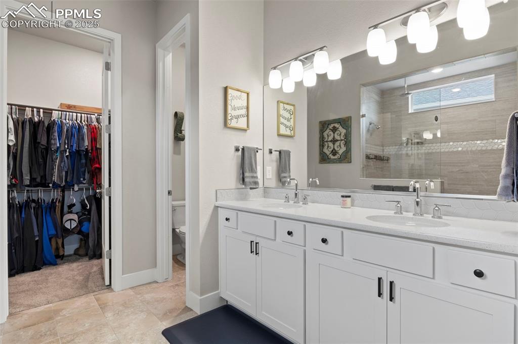 Image 16 of 38: Full bathroom with a walk in closet, double vanity, a sink, and tiled showe