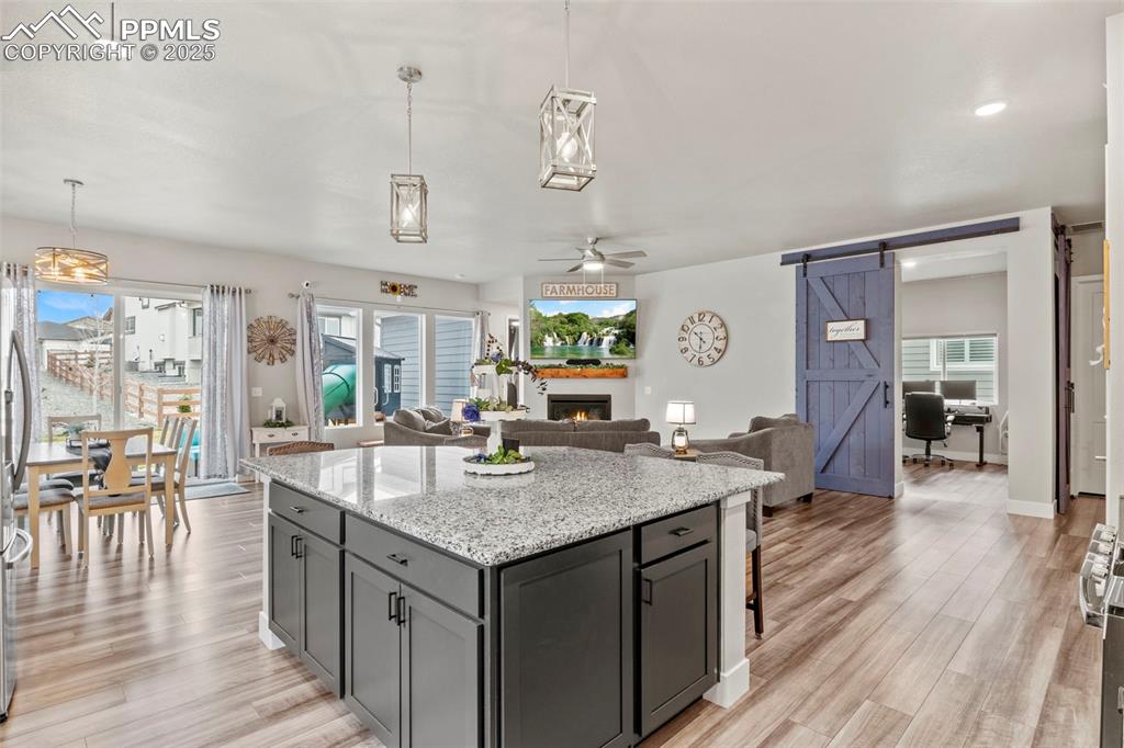 Image 3 of 38: Kitchen with a barn door, ceiling fan, light wood-style floors, and a warm