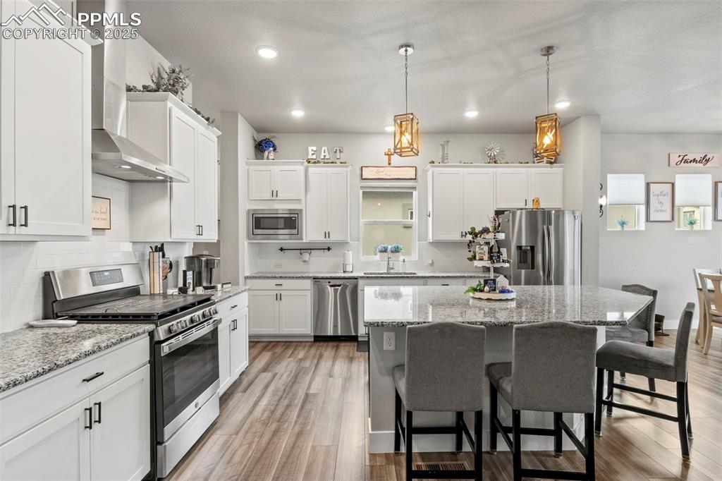 Image 5 of 38: Kitchen with wall chimney range hood, a kitchen breakfast bar, white cabine