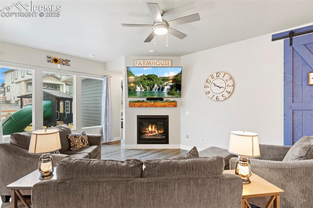 Image 7 of 38: Living room with a barn door, wood finished floors, ceiling fan, and a glas