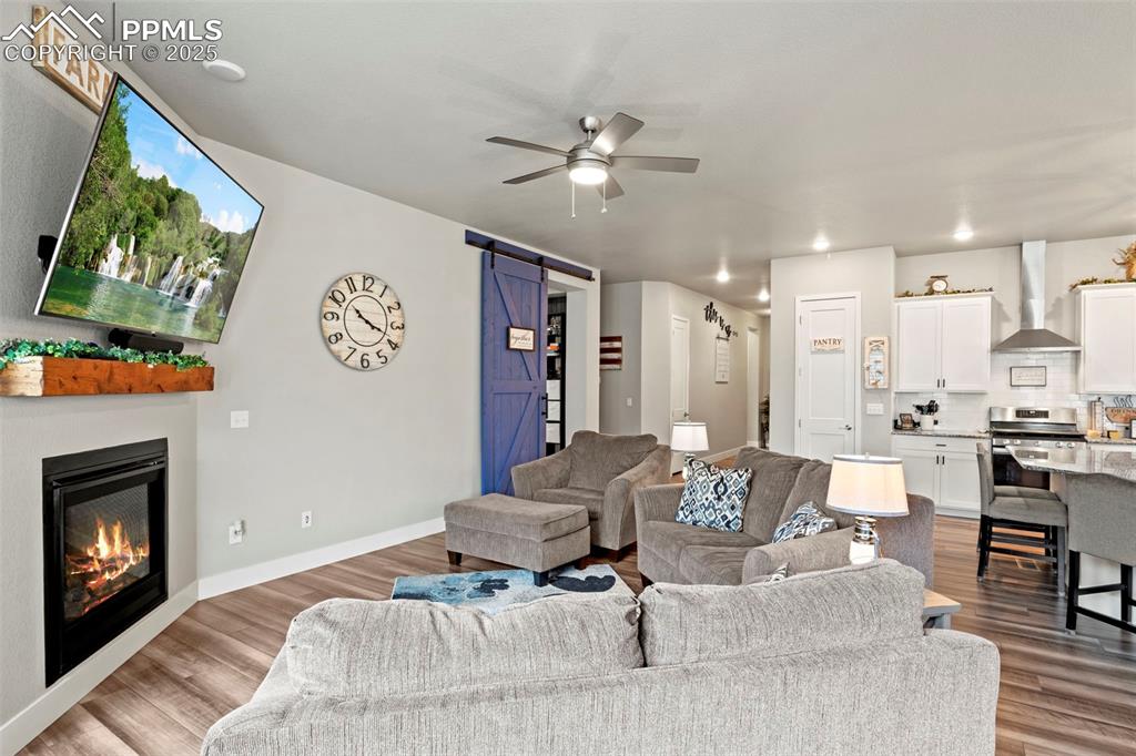 Image 8 of 38: Living room with a barn door, wood finished floors, a ceiling fan, and a gl