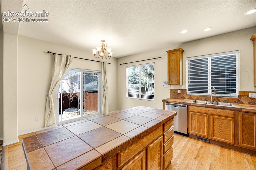 Image 14 of 39: Kitchen featuring wood cabinetry, tile countertops, stainless steel dishwas