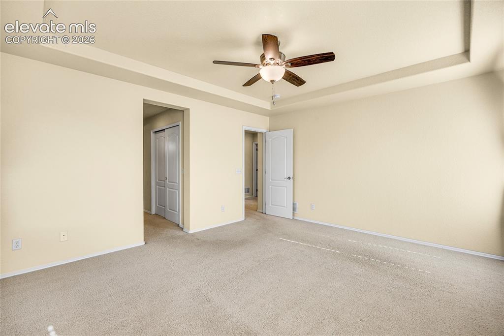 Image 18 of 39: Spacious room featuring a tray ceiling with a ceiling fan, neutral carpet f