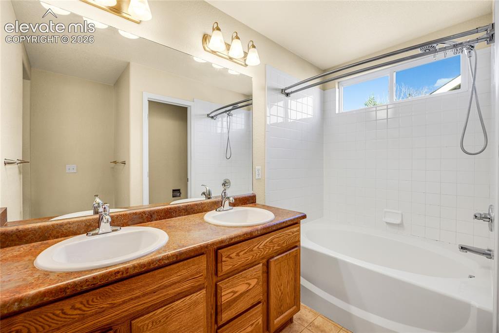 Image 20 of 39: Bathroom featuring a double vanity with wood-finish cabinetry, a large mirr