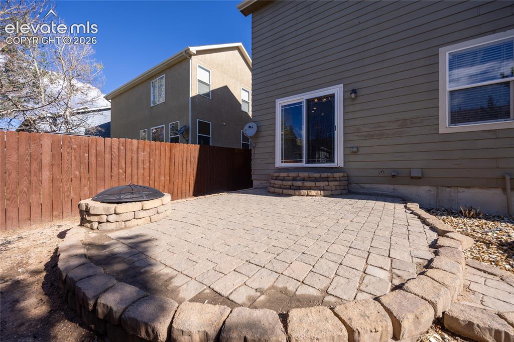 Image 32 of 39: Backyard patio featuring paver stones, a stone fire pit, wood fence, and sl