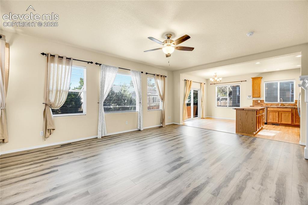 Image 7 of 39: Spacious living area featuring light wood-finish flooring, a ceiling fan, a