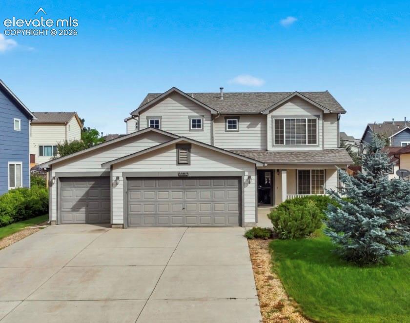 Caption: Two-story residence featuring light gray siding, a prominent two-car garage, and a covered front por
